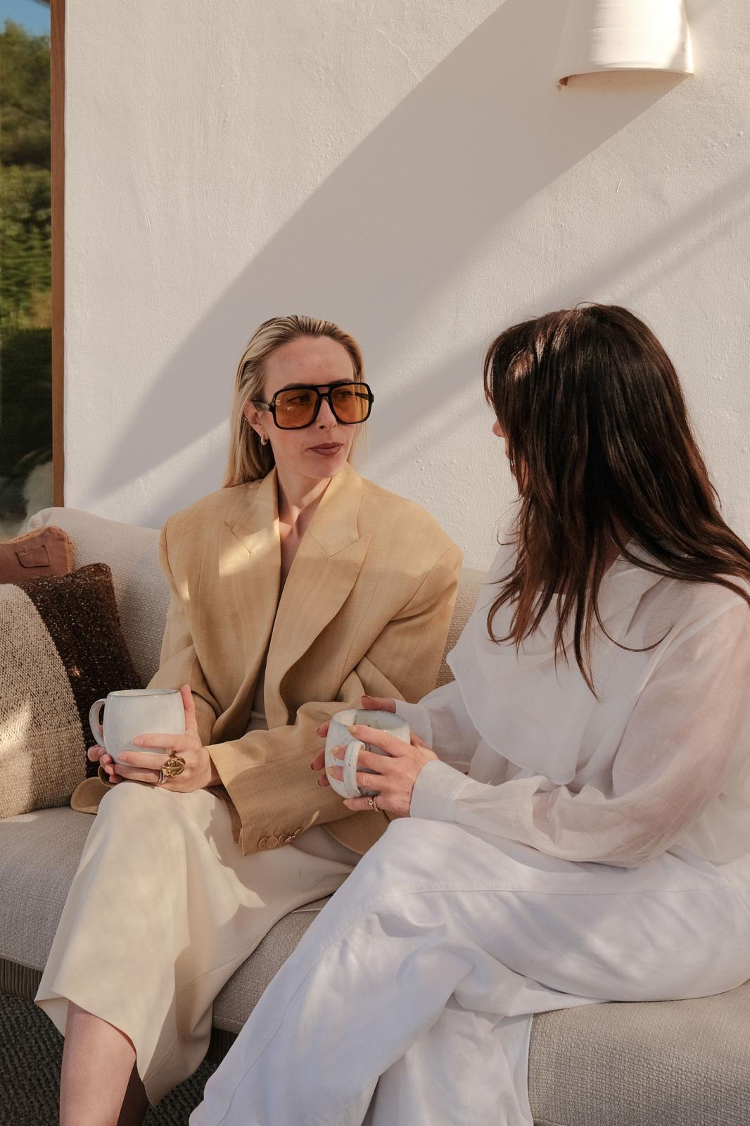 Vrouw in beige in gesprek met Hanneke Peeters in het wit, met een mok in de hand
